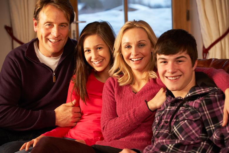 Older couple with older children sitting on their living room couch smiling